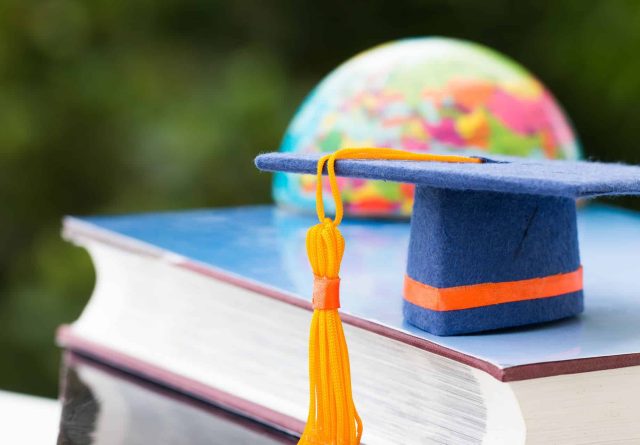 Graduate or Education knowledge learning study abroad concept : Blue Graduation cap on textbook with blur of europe earth world globe , blur green light background. Back to School